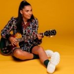 portrait de l'artiste française Camille Esteban et sa guitare sur fond orange
