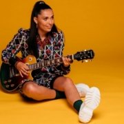 portrait de l'artiste française Camille Esteban et sa guitare sur fond orange