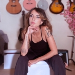 portrait de l'artiste Alba assise et avec des guitares accrochées au mur