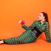 portrait de l'artiste Alexandra Miller allongée au sol se maintenant sur une main sur un fond orange