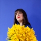 portrait sur fond bleu de l'artiste June Mio tenant un gros bouquet jaune