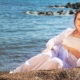 l'artiste Alexandra Miller est couché sur le côté le buste relevé sur une plage habillée en blanc
